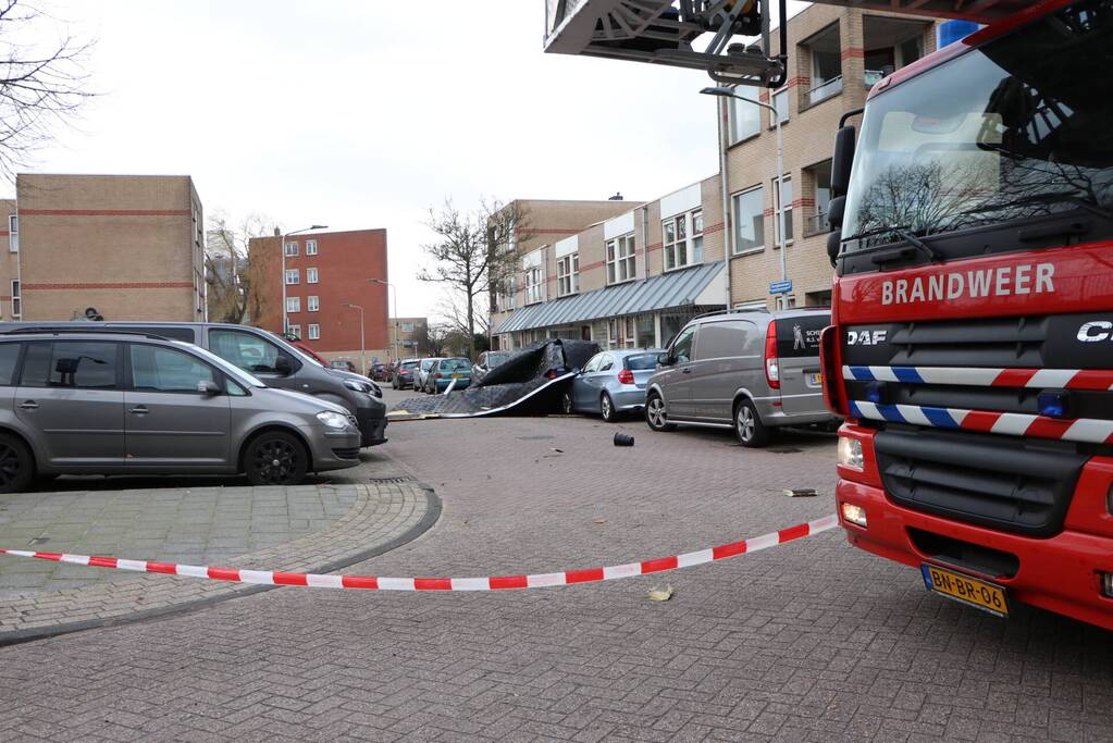 Dakbedekking van flat waait over auto's en lantaarnpalen