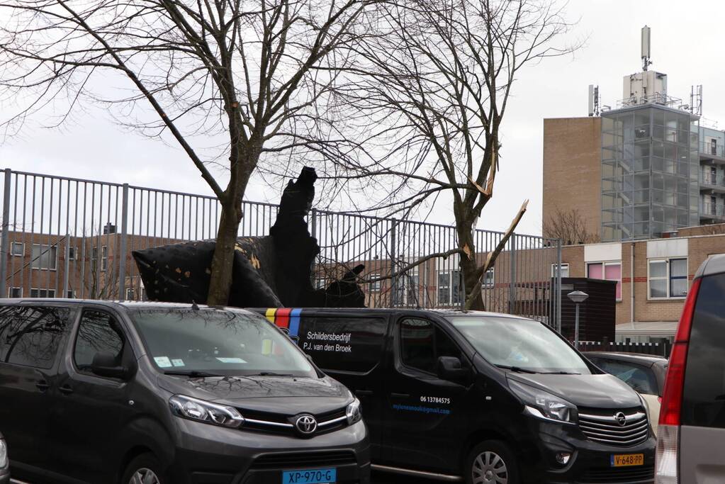 Dakbedekking van flat waait over auto's en lantaarnpalen