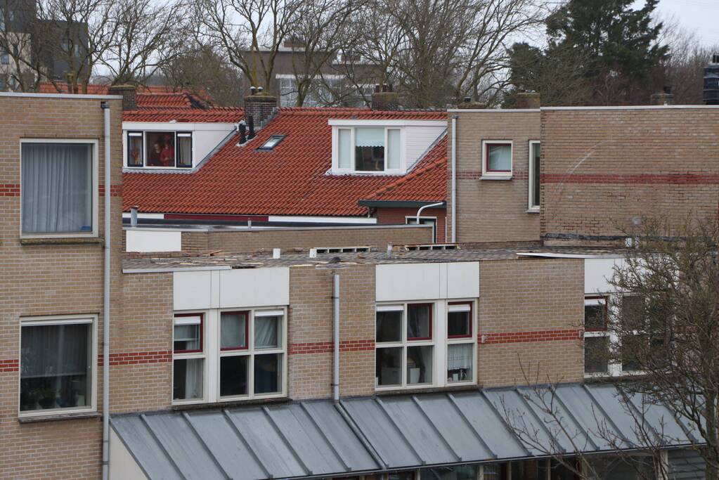 Dakbedekking van flat waait over auto's en lantaarnpalen