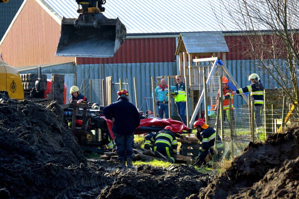 Persoon bekneld onder omgevallen graafmachine