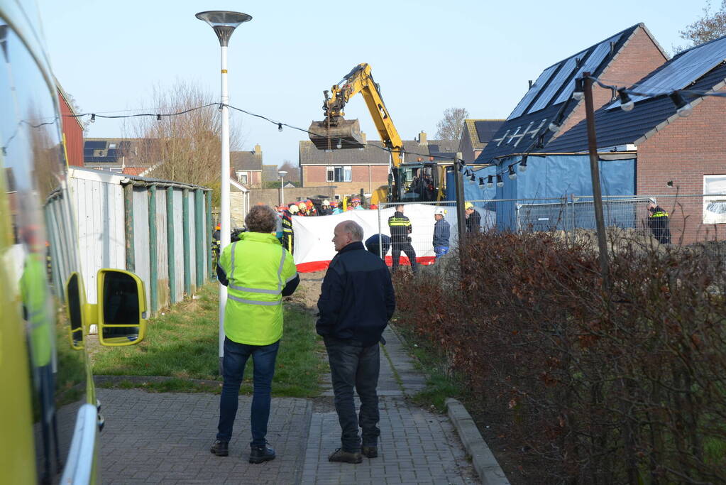 Persoon bekneld onder omgevallen graafmachine