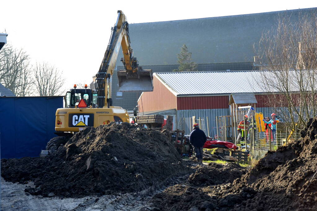 Persoon bekneld onder omgevallen graafmachine