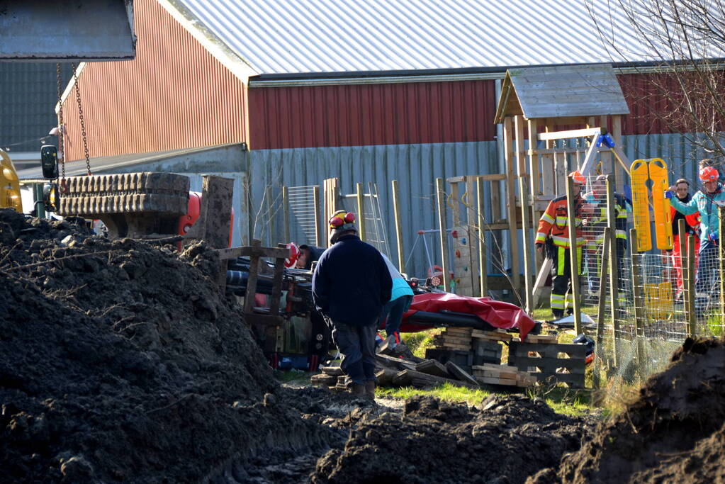 Persoon bekneld onder omgevallen graafmachine