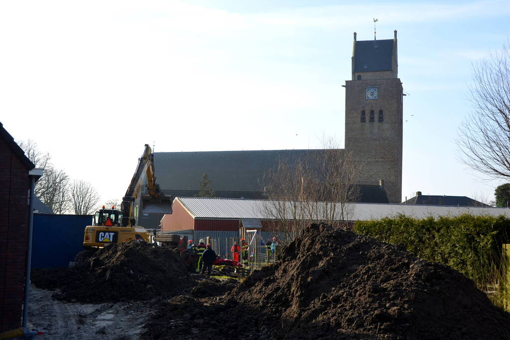 Persoon bekneld onder omgevallen graafmachine