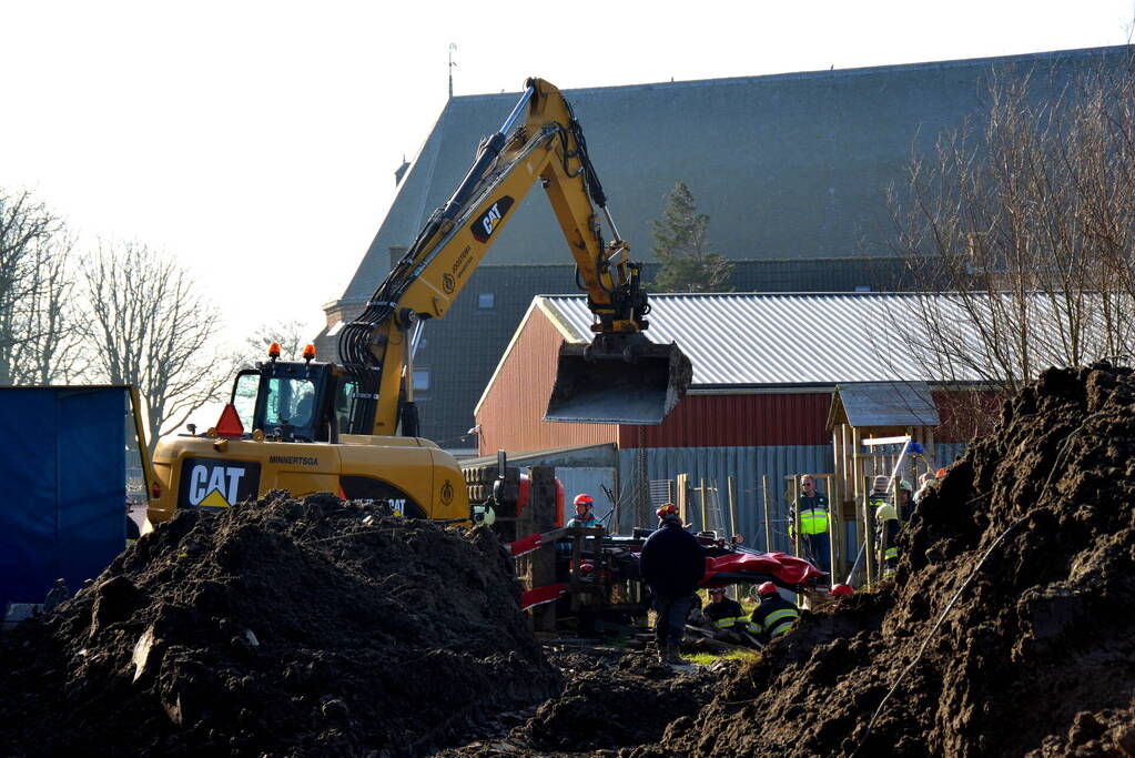 Persoon bekneld onder omgevallen graafmachine