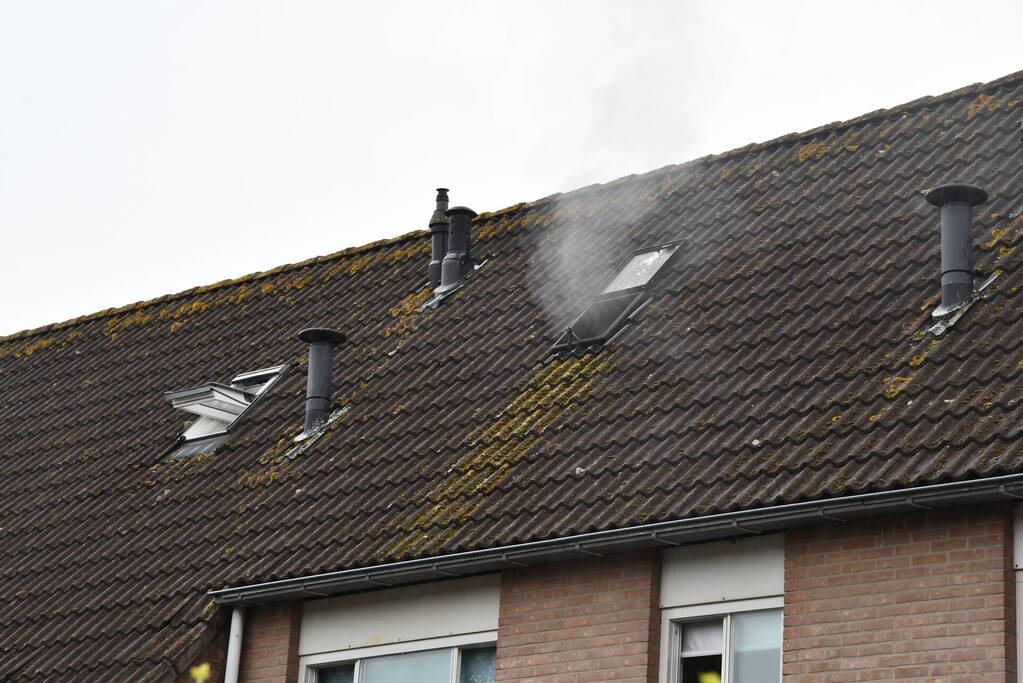 Veel rook uit zolderraam bij brand in woning