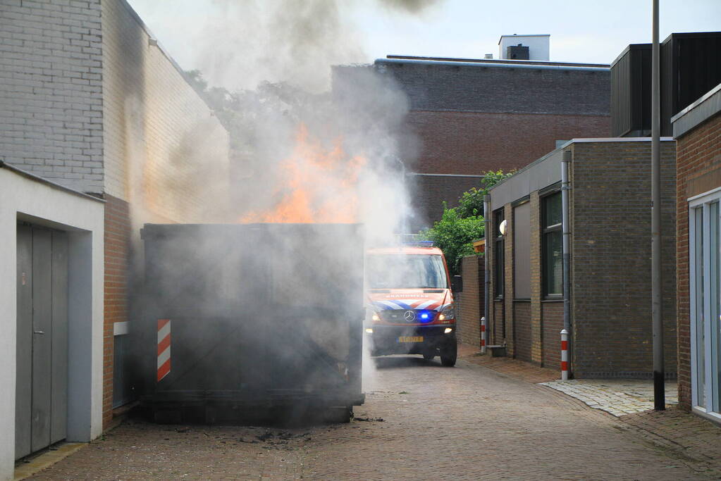 Vlammen slaan uit bouwcontainer met afval