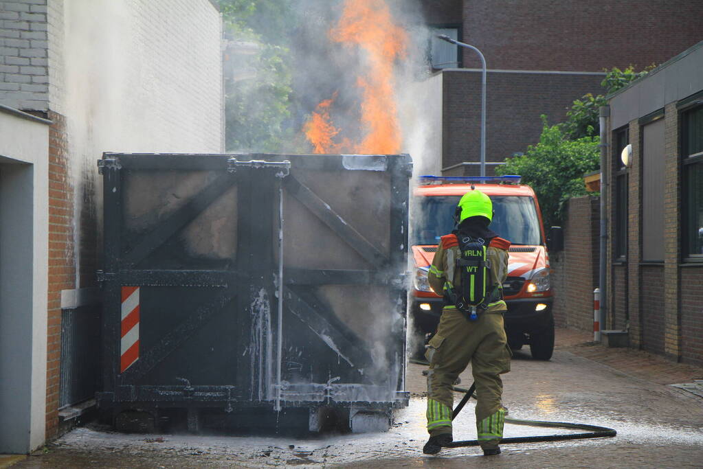 Vlammen slaan uit bouwcontainer met afval