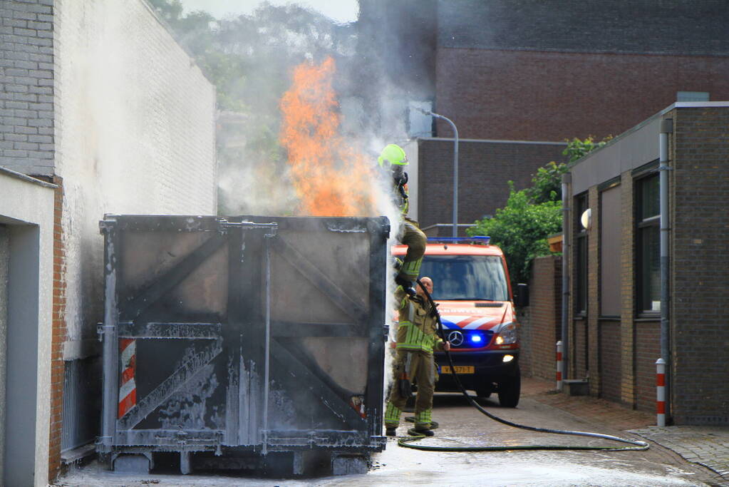 Vlammen slaan uit bouwcontainer met afval