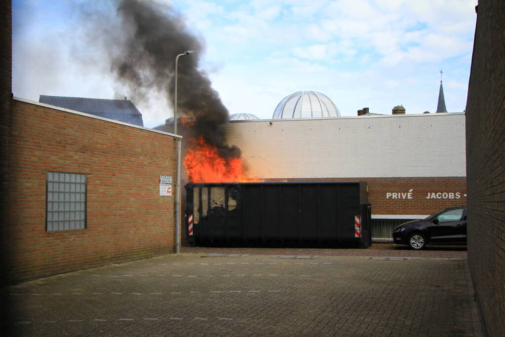 Vlammen slaan uit bouwcontainer met afval