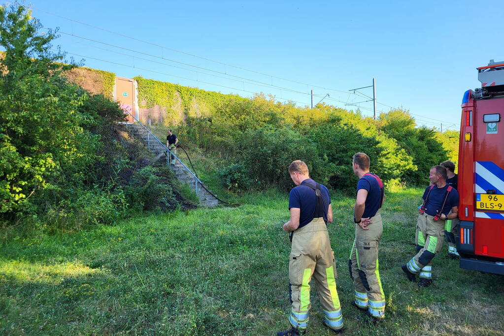 Brandweer blust bermbrand naast treinspoor