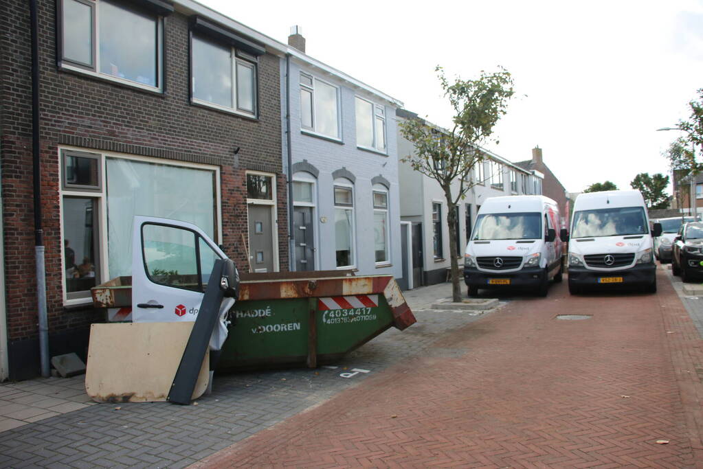Pakketbezorger botst tegen bouwcontainer en knalt tegen woning