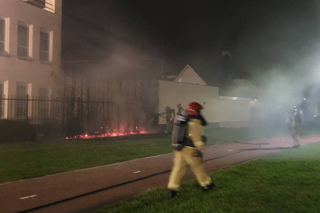Brandweer blust brandend heg naast pand