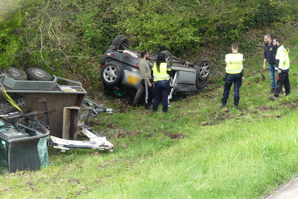 Auto en aanhanger met graafmachine over de kop
