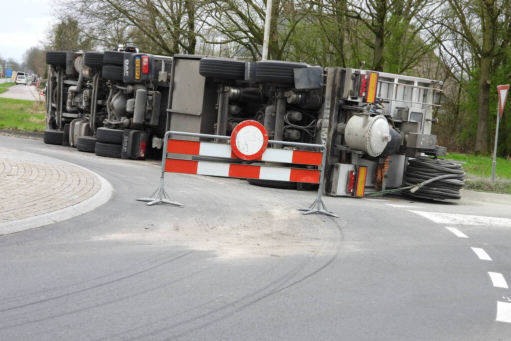 Vrachtwagencombinatie met zand kantelt op rotonde
