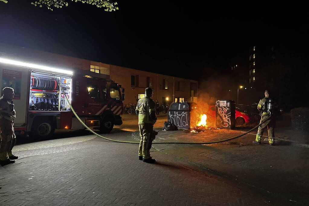 Brandweer blust brandend afval naast container