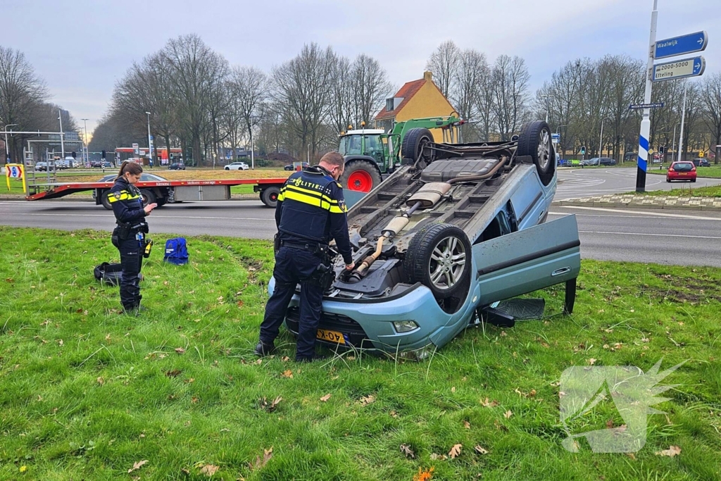 Auto belandt op kop naast rotonde