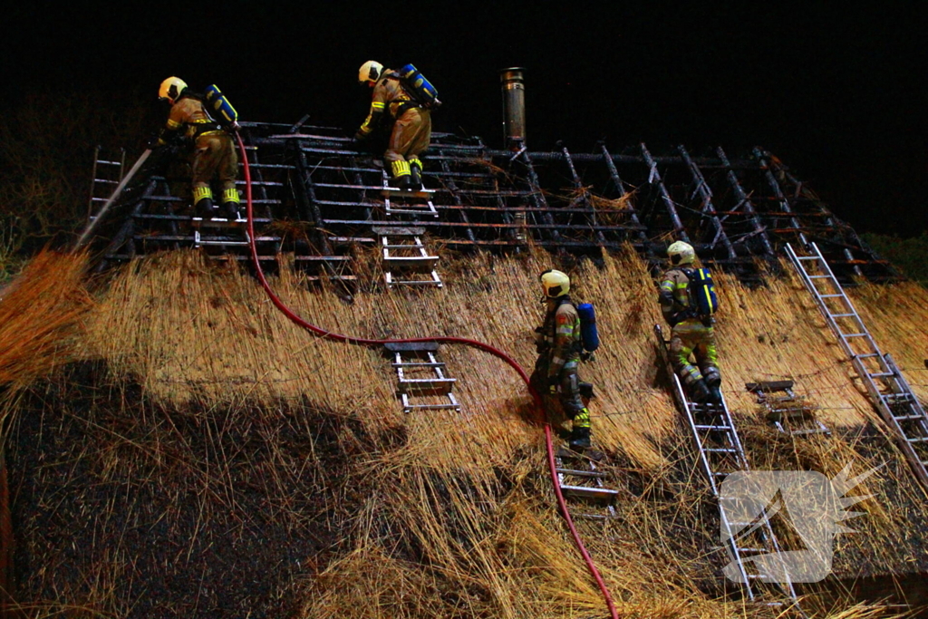 Brandweerlieden trekken rietendak uit elkaar om brand te kunnen bestrijden