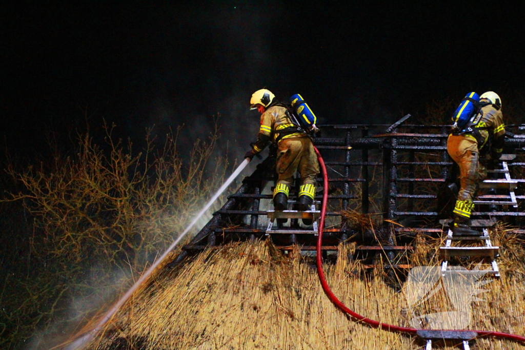 Brandweerlieden trekken rietendak uit elkaar om brand te kunnen bestrijden