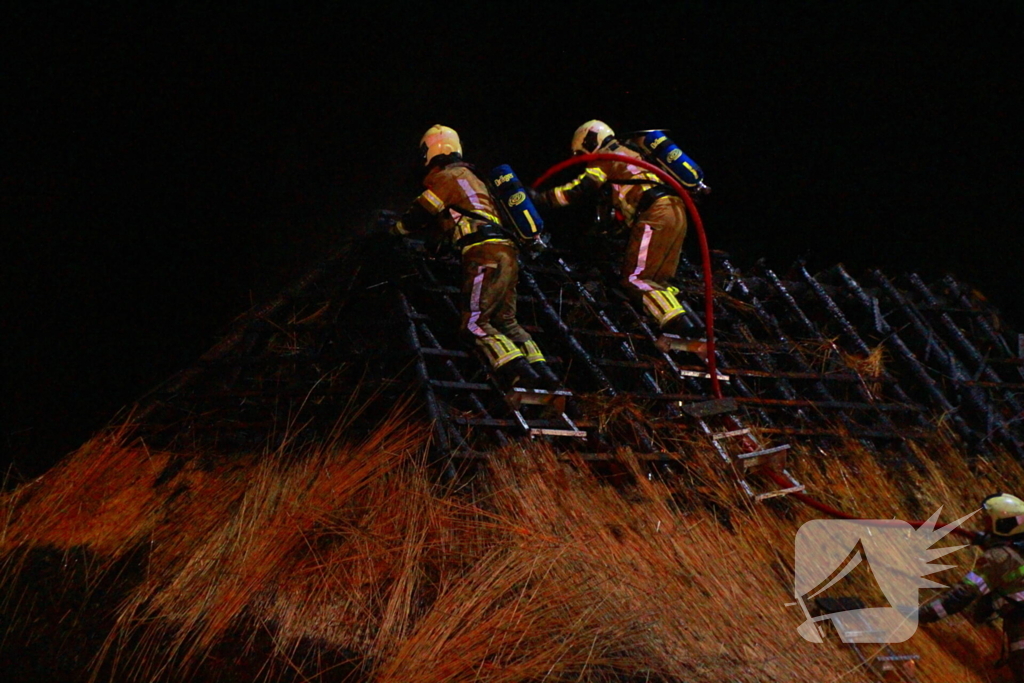 Brandweerlieden trekken rietendak uit elkaar om brand te kunnen bestrijden