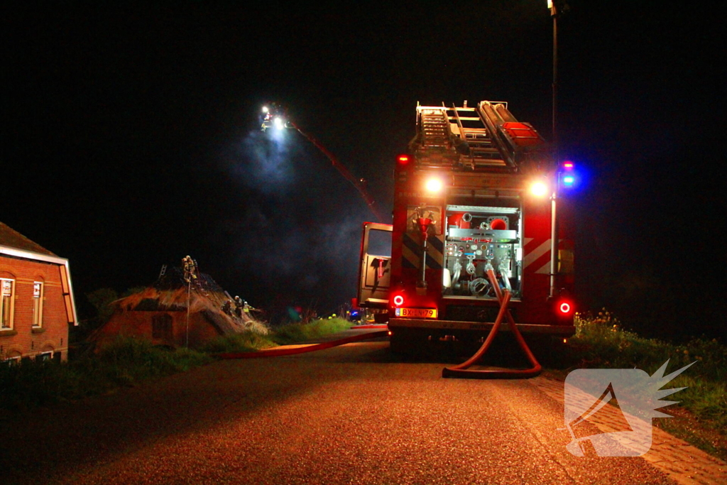 Brandweerlieden trekken rietendak uit elkaar om brand te kunnen bestrijden