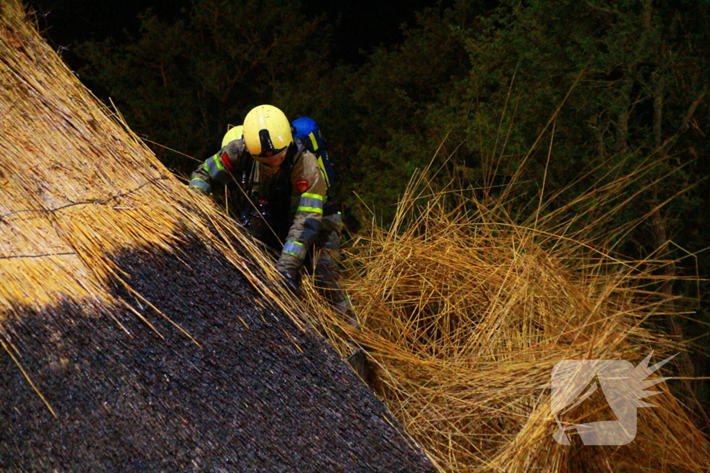Brandweerlieden trekken rietendak uit elkaar om brand te kunnen bestrijden