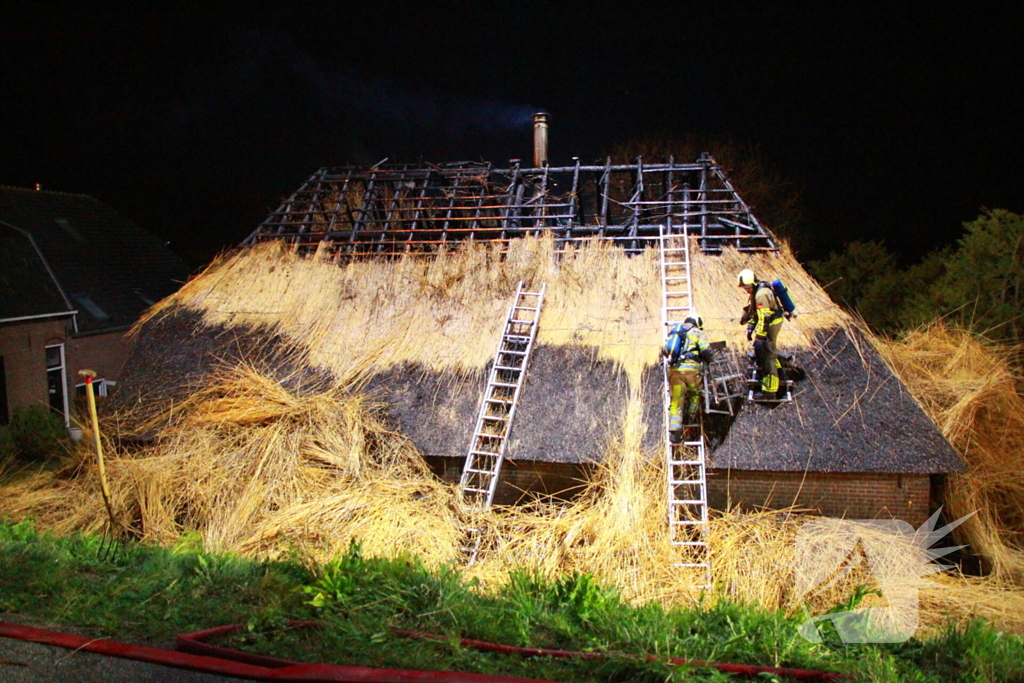 Brandweerlieden trekken rietendak uit elkaar om brand te kunnen bestrijden