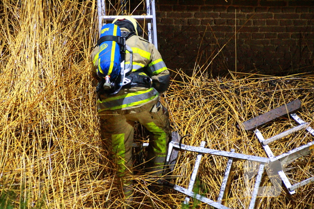 Brandweerlieden trekken rietendak uit elkaar om brand te kunnen bestrijden