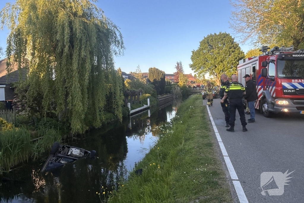 Auto belandt op de kop in het water, omstanders verrichten redding