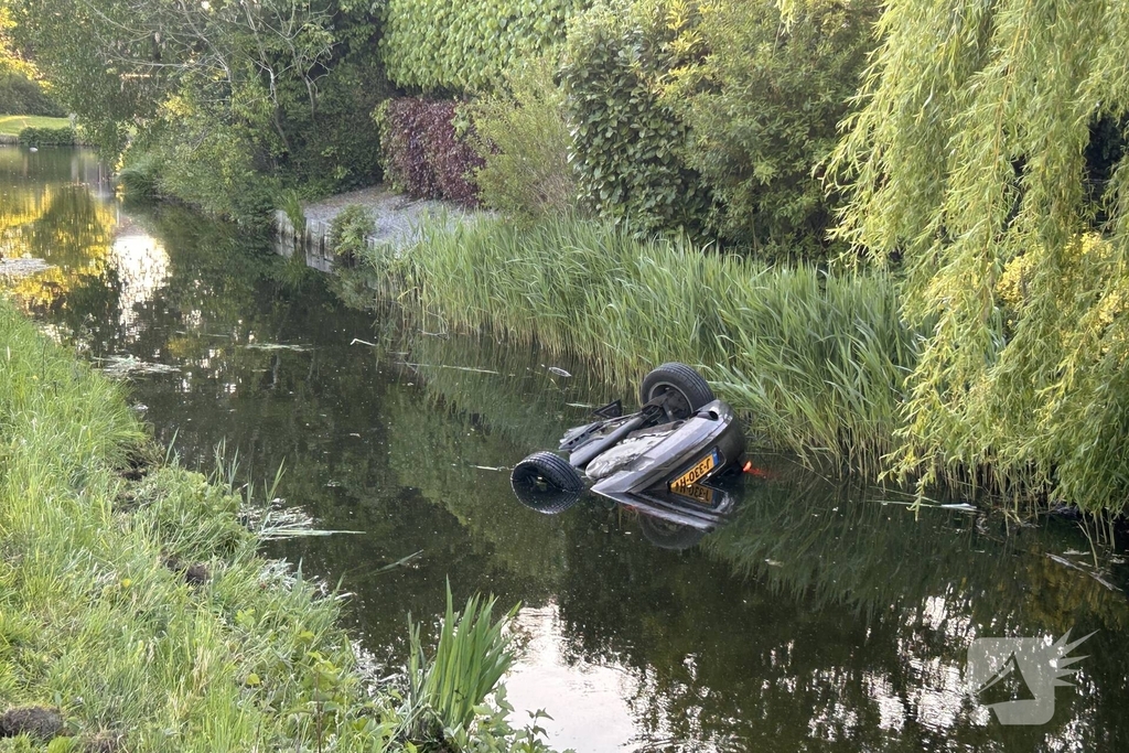 Auto belandt op de kop in het water, omstanders verrichten redding