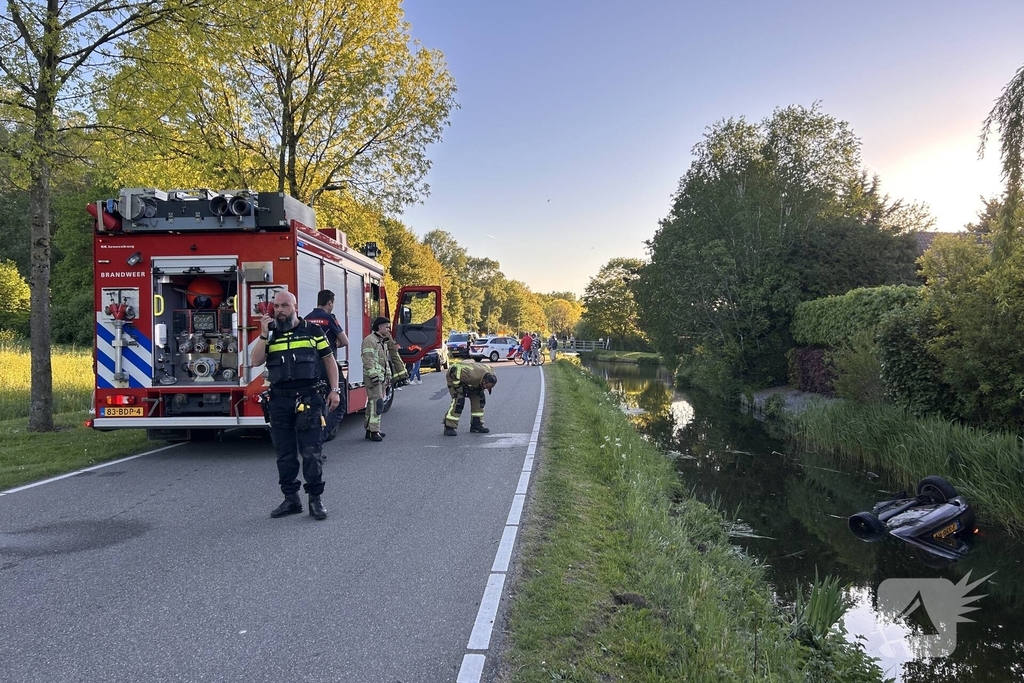 Auto belandt op de kop in het water, omstanders verrichten redding