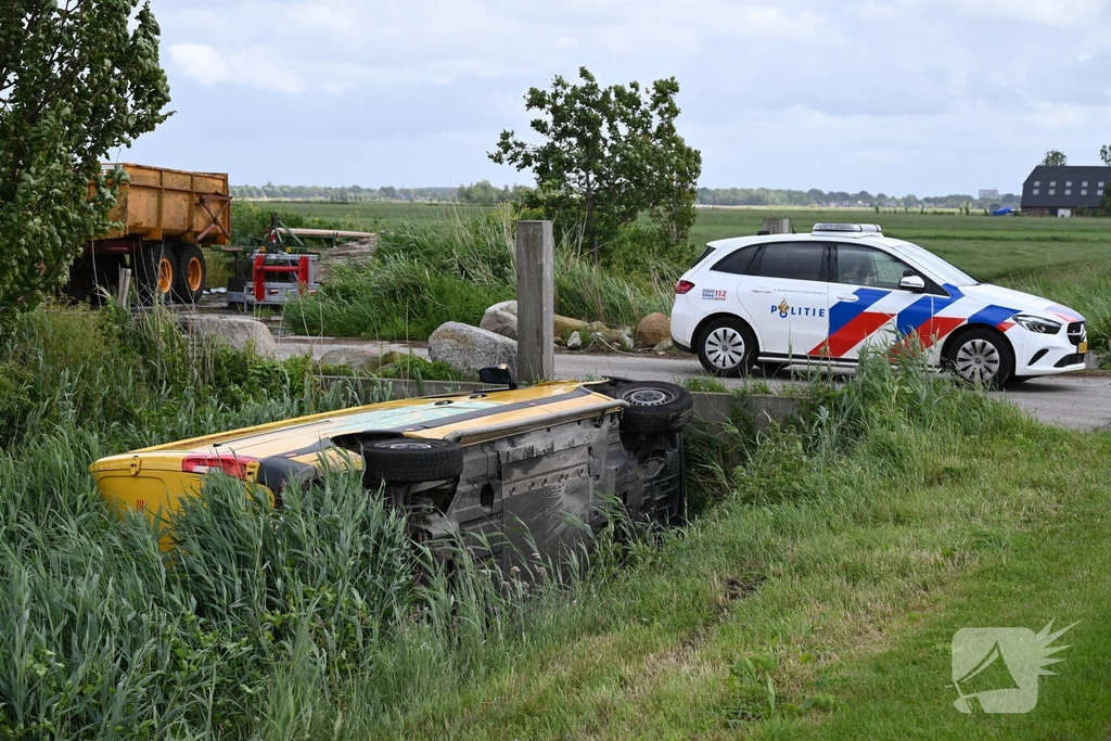 Bus van pakketdienst belandt op zijkant in sloot