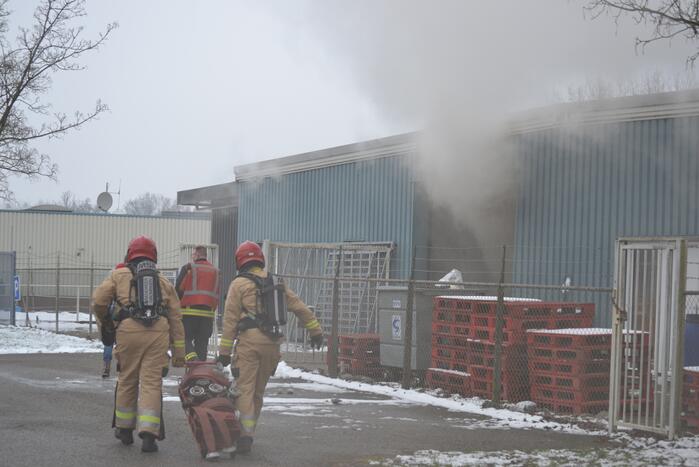 Houtopslag tegen loods aan vat vlam