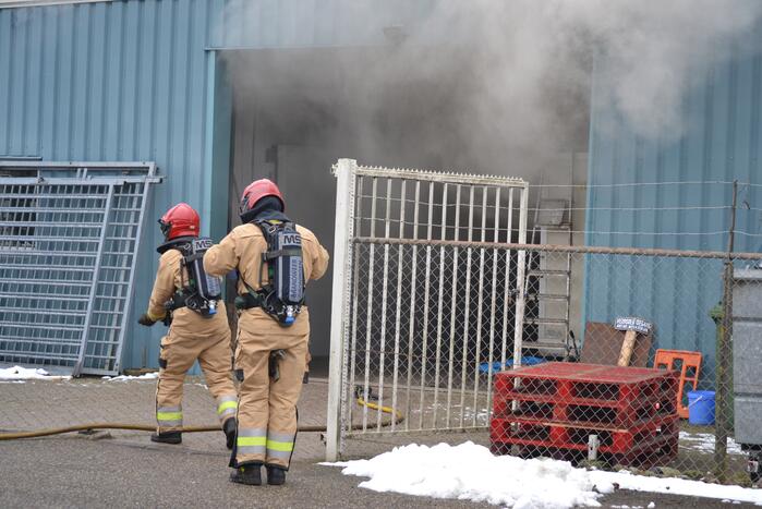 Houtopslag tegen loods aan vat vlam