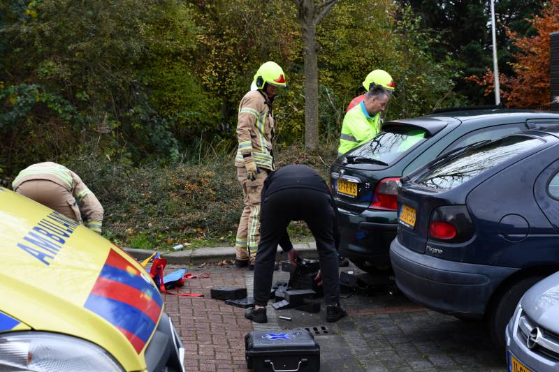 Persoon bekneld onder auto