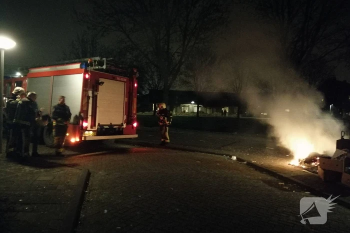 Vuurwerkresten in de brand naast papiercontainer