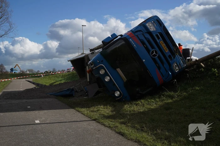 Vrachtwagen met zand van dijk gekanteld