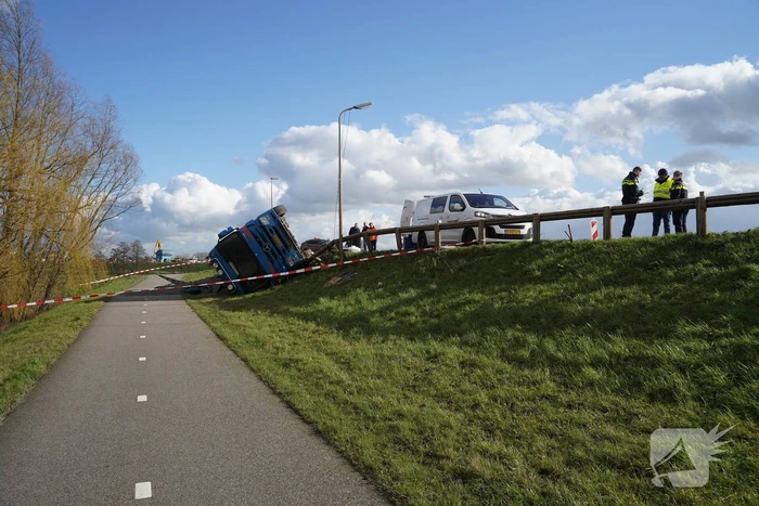 Vrachtwagen met zand van dijk gekanteld