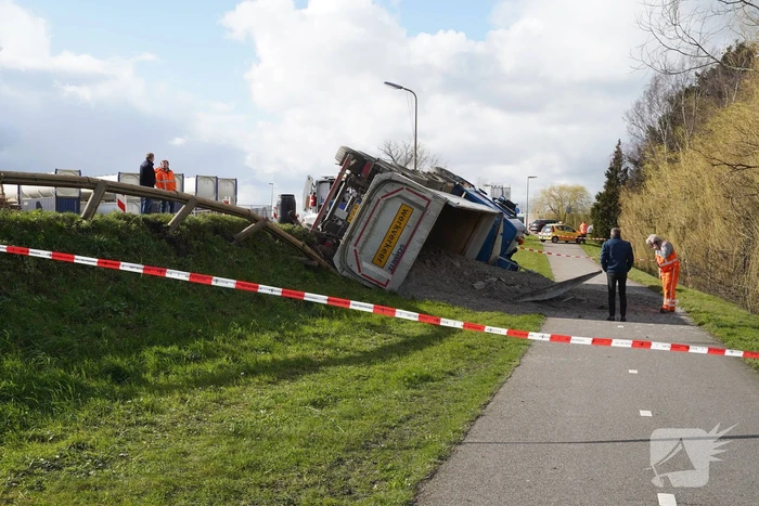 Vrachtwagen met zand van dijk gekanteld