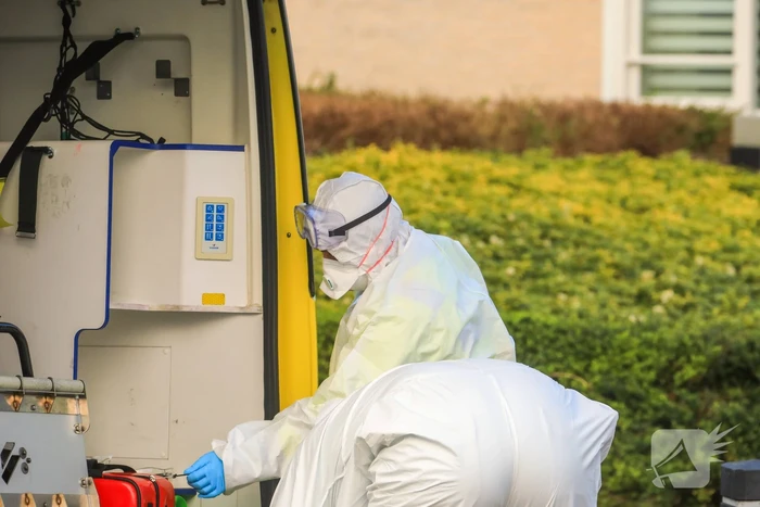Mannen in witte pakken halen vermoedelijke coronapatiënt uit huis