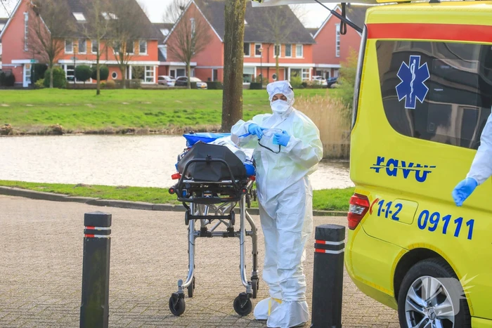 Mannen in witte pakken halen vermoedelijke coronapatiënt uit huis