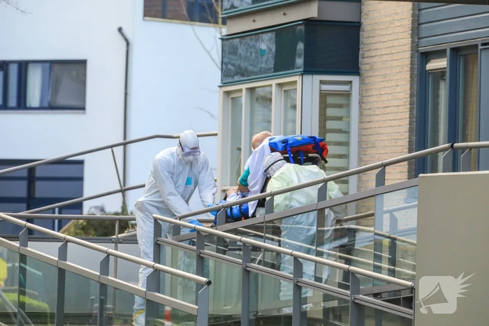 Mannen in witte pakken halen vermoedelijke coronapatiënt uit huis