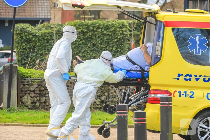 Mannen in witte pakken halen vermoedelijke coronapatiënt uit huis