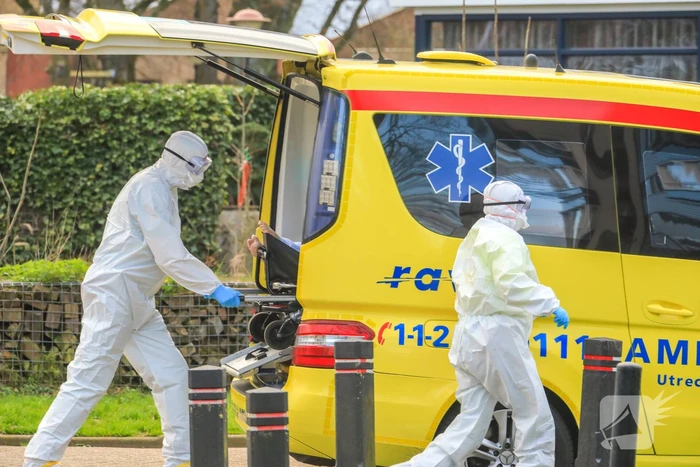 Mannen in witte pakken halen vermoedelijke coronapatiënt uit huis