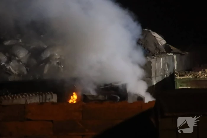 Grote berg afvalhout in brand naast houtopslag
