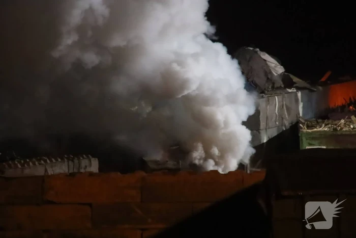 Grote berg afvalhout in brand naast houtopslag
