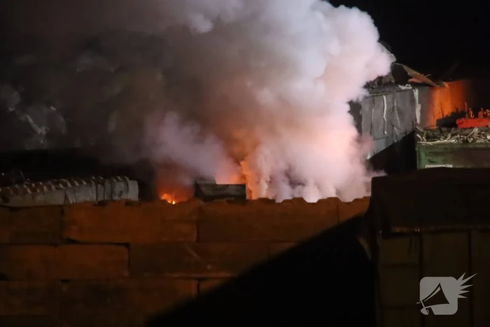 Grote berg afvalhout in brand naast houtopslag