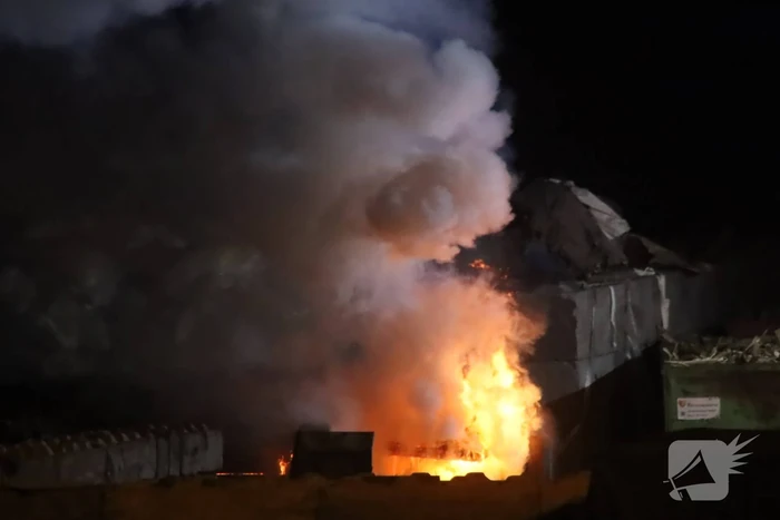 Grote berg afvalhout in brand naast houtopslag
