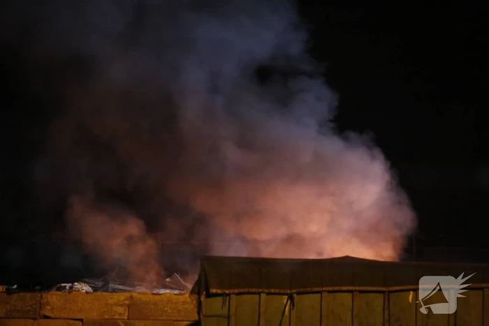 Grote berg afvalhout in brand naast houtopslag