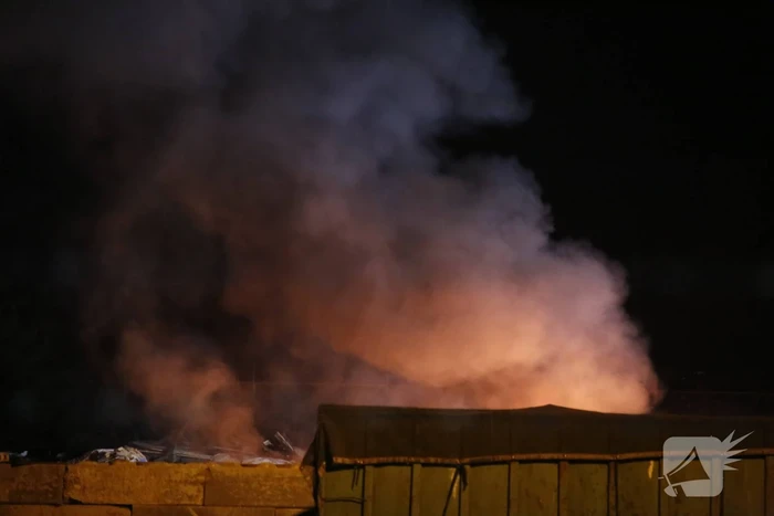 Grote berg afvalhout in brand naast houtopslag